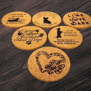 May include: A collection of six round cork coasters with black text and graphics. The coasters feature dog-related phrases and images, including a paw print heart, a dog silhouette, and the words "Live Love Bark."