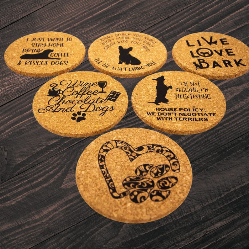 May include: A collection of six round cork coasters with black text and graphics. The coasters feature dog-related phrases and images, including a paw print heart, a dog silhouette, and the words "Live Love Bark."