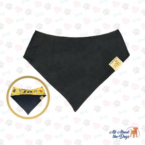 May include: Black dog bandana with a yellow and white pattern of dogs on the edges. The bandana has a small brown label with a dog silhouette on it. The text "All About the Dogs" is printed in white on a brown background.