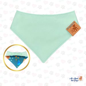 May include: A mint green dog bandana with a stitched edge and a brown leather tag. An additional bandana with a floral pattern is shown in a gold circle. The tag reads "All About the Dogs".