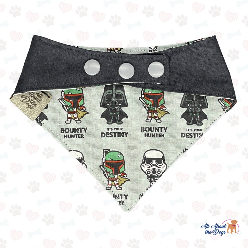 May include: A black and white dog bandana with a Star Wars theme. The bandana features a repeating pattern of Darth Vader, Boba Fett, and Stormtrooper characters. The bandana has a black adjustable strap with three white snaps.