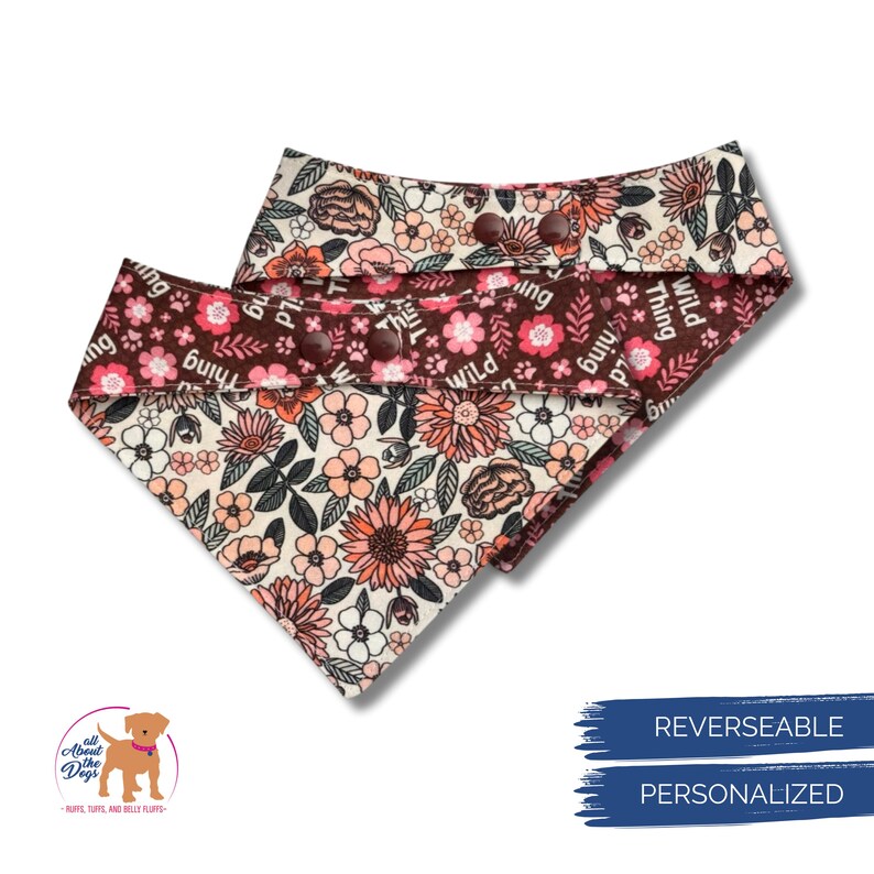 May include: Two reversible dog bandanas with floral patterns in shades of pink, peach, brown, and cream. One bandana has the text "Wild Thing" and the other has the text "Wild Thing" repeated. Each bandana has brown buttons.