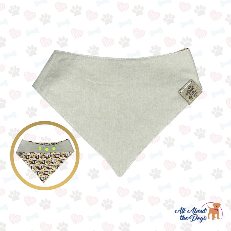 May include: A light grey dog bandana with a brown leather tag that says "All About the Dogs". The bandana is on a white background with a pattern of hearts, paw prints, and bones.