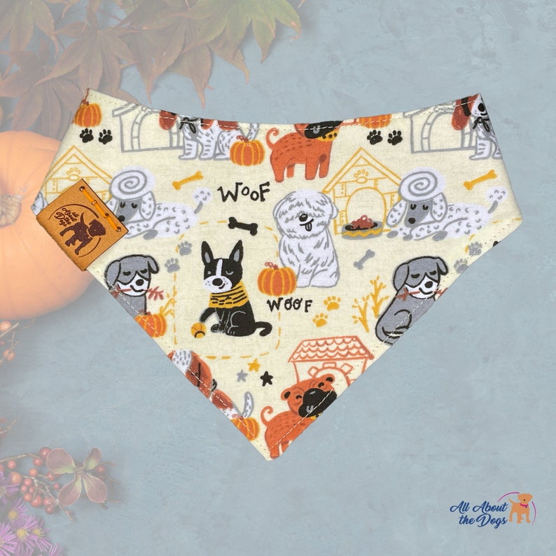 Pu&ograve; includere: Bandana color crema per cani con un motivo ripetuto di cani, zucche, cucce e ossa. La parola "Woof" &egrave; stampata in arancione. &Egrave; attaccata una piccola etichetta in pelle con la silhouette di un cane.