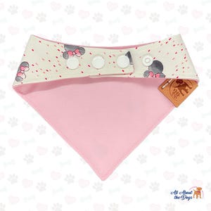 May include: A pink and white dog bandana with a playful design. The top band features a pattern of gray mouse heads with pink bows and red dots. The bandana has three white snap closures and a pink triangle bottom. A brown tag reads "All About the Dogs".