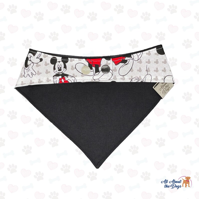 May include: A black and white dog bandana featuring a Mickey Mouse design. The top section has a light grey background with Mickey Mouse illustrations and a red and black design. The bottom section is solid black. The bandana has a button closure.