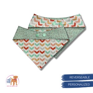 May include: Two reversible dog bandanas. One bandana features a mint green polka dot pattern on the reverse side and a chevron pattern in red, gold, and mint green on the front. The other bandana has a similar chevron pattern and a mint green polka dot pattern.