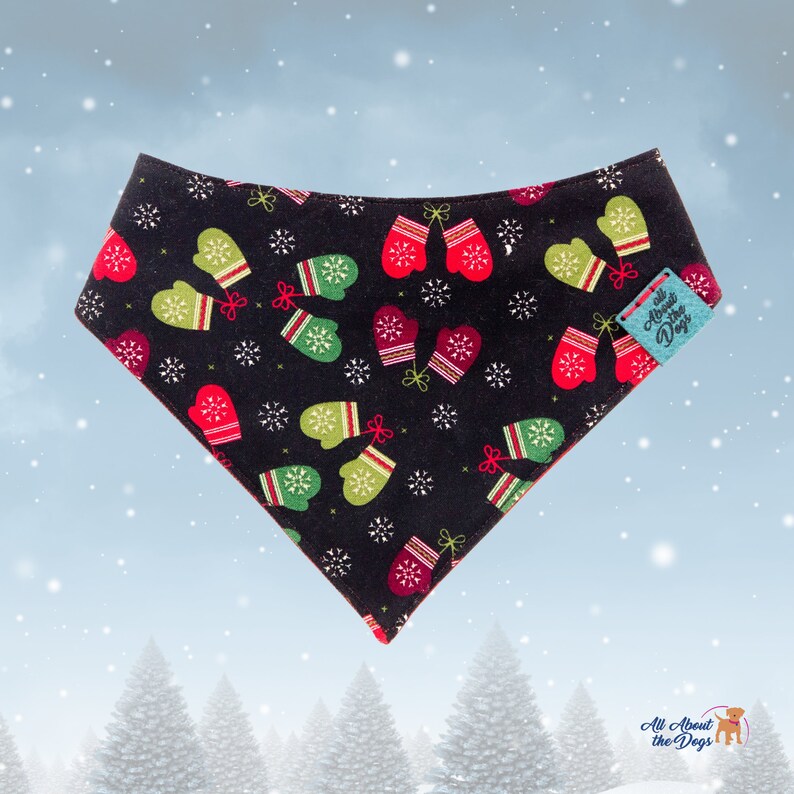 May include: Black dog bandana with a festive pattern of red and green mittens and white snowflakes. The bandana has a red border and a small tag that says "All About the Dogs". A winter-themed accessory for pets.