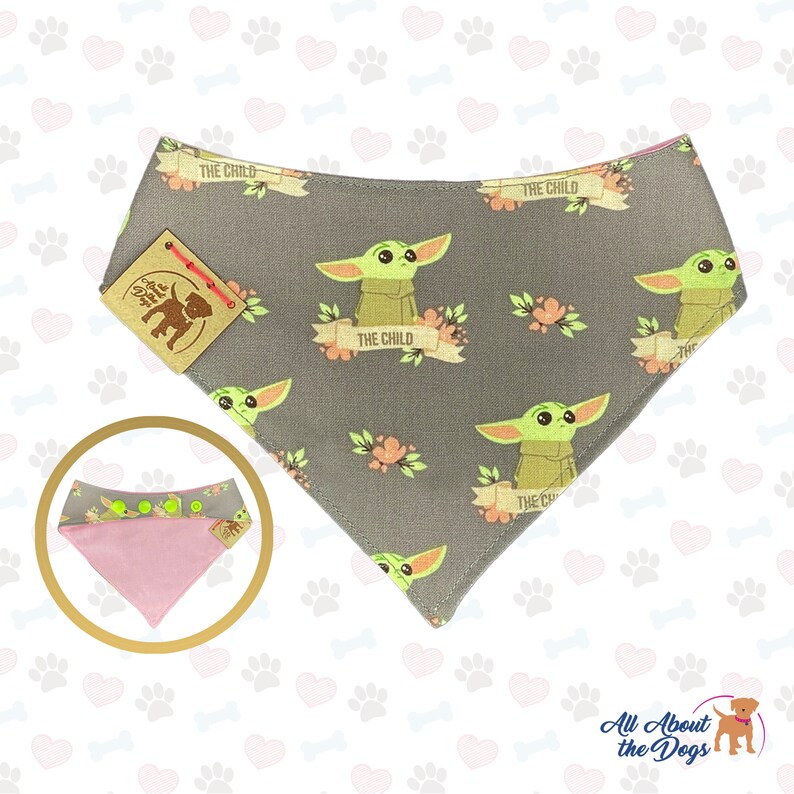 Puede incluir: Un bandana para perro gris y rosa con un patr&oacute;n repetido de un personaje alien&iacute;gena verde con el texto "The Child" en una pancarta. El bandana tiene una parte inferior rosa y una etiqueta marr&oacute;n con una silueta de perro.