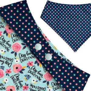 May include: Dog bandana with a navy blue polka dot pattern and a light blue floral pattern. The bandana has the text "Dog hair don't care" printed on it. The bandana has two white snaps.