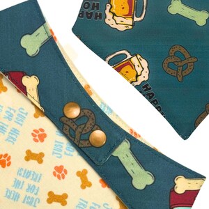 K&ouml;nnte beinhalten: Hunde-Bandana und -Halsband-Set in Teal und Creme. Der teal Stoff zeigt Bierkr&uuml;ge, Brezeln und Knochen-Illustrationen. Der cremefarbene Stoff hat Pfotenabdr&uuml;cke, Knochen und den Text "Just Here For The Treats!"