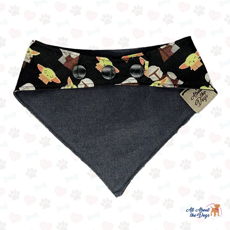 May include: Black and green dog bandana with a pattern of cartoon baby Yoda characters. The bandana has a black snap closure and a brown leather tag that says "All About the Dogs".