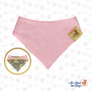 Puede incluir: Bandana rosa para perro con un patr&oacute;n verde y marr&oacute;n que presenta un personaje de dibujos animados. La bandana est&aacute; hecha de algod&oacute;n y tiene un cierre de broche. La bandana se muestra sobre un fondo blanco con un patr&oacute;n de corazones y huellas de patas.