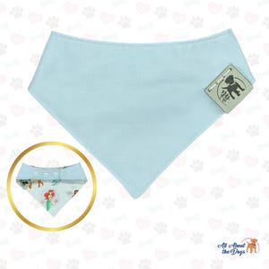 Peut inclure: Un bandana bleu clair pour chien, de forme triangulaire. Le bandana porte une &eacute;tiquette avec l'inscription "All About the Dogs". Un bandana plus petit avec une impression color&eacute;e d'une sir&egrave;ne et d'autres personnages est &eacute;galement visible.