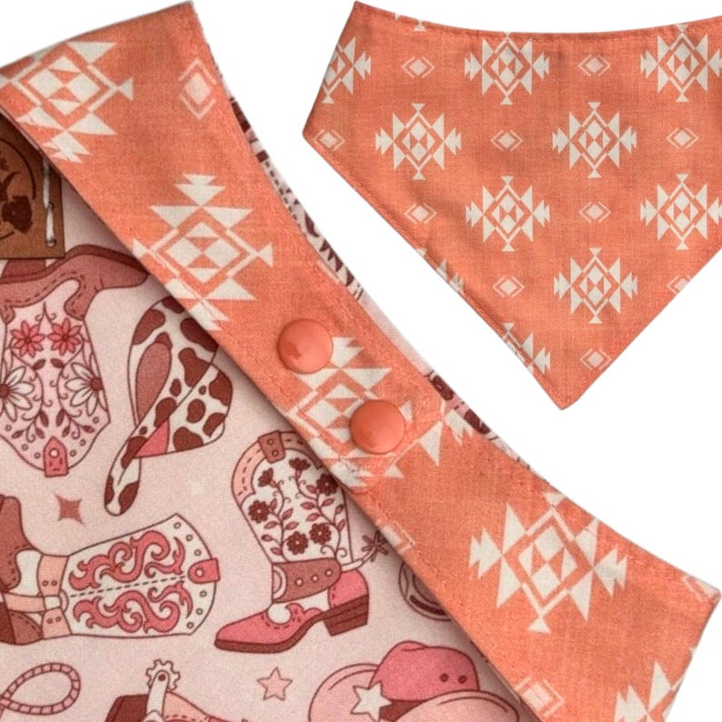 Może przedstawiać: Zestaw bandany i śliniaka dla psa. Bandana ma kształt tr&oacute;jkąta z geometrycznym wzorem w stylu południowo-zachodnim w kolorze brzoskwiniowym i białym. Śliniak ma brzoskwiniową obw&oacute;dkę z dwoma brzoskwiniowymi guzikami i wzorem kowbojskich but&oacute;w, kapeluszy i innych zachodnich wzor&oacute;w.