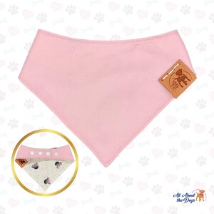May include: A light pink dog bandana with a triangular shape. The bandana has a stitched edge and a small brown leather tag with a dog silhouette. A smaller bandana with a Minnie Mouse pattern is shown in a gold circle.