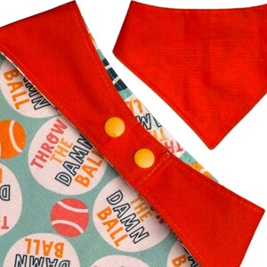Peut inclure: Bandana pour chien avec une bordure rouge et deux fermetures &agrave; bouton-pression jaunes. Le bandana pr&eacute;sente un motif bleu clair avec des balles de tennis et le texte "THROW THE DAMN BALL". Un bandana rouge uni s&eacute;par&eacute; est &eacute;galement visible.