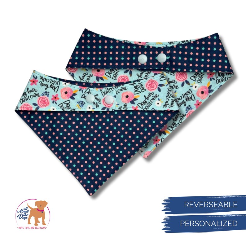 May include: Two reversible dog bandanas. One side features a navy blue polka dot pattern, the other a light blue floral design with pink roses and the text "Dog hair, don't care." Each bandana has white snap closures.