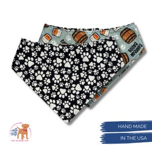 May include: Two dog bandanas. One is black with white paw prints. The other is light blue with bourbon barrel and glass designs. The words "Bourbon Buddy" are printed on the light blue bandana. The bandanas are hand made in the USA.