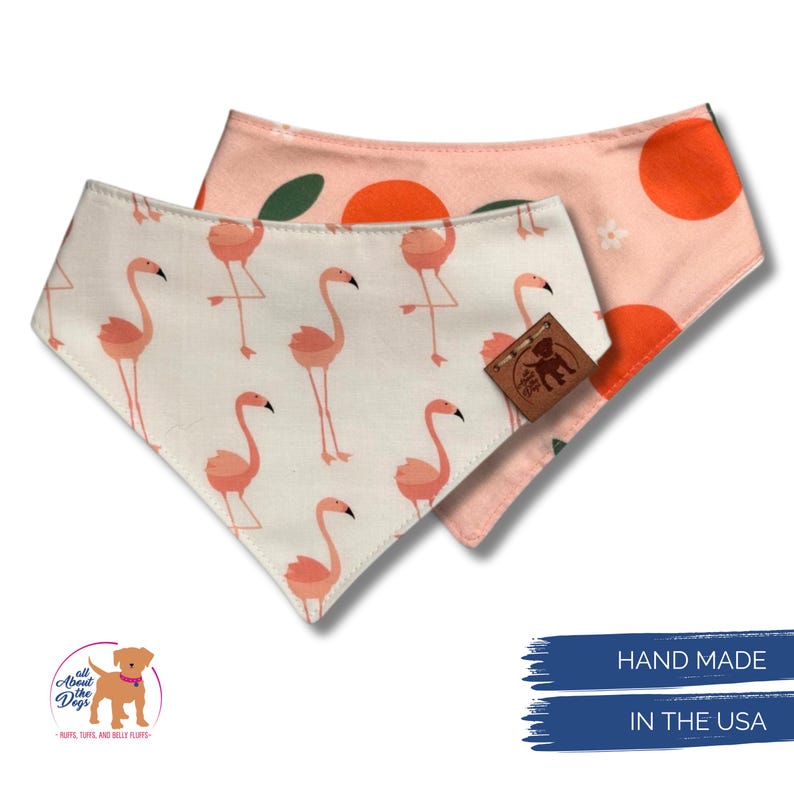 May include: Two dog bandanas. One is white with pink flamingos. The other is pink with orange circles and green leaves. A brown leather tag is attached to the bandanas. Text on the tag reads "All About Dogs". Text at the bottom reads "Hand Made In The USA".