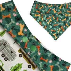 Op de afbeelding: Hondenbandana met een groene achtergrond en een patroon van oranje en lichtgroene botten, roze hartjes en zwarte pootafdrukken. De bandana heeft een bijpassende verstelbare kraag met groene drukknopen en een kampeerthema.