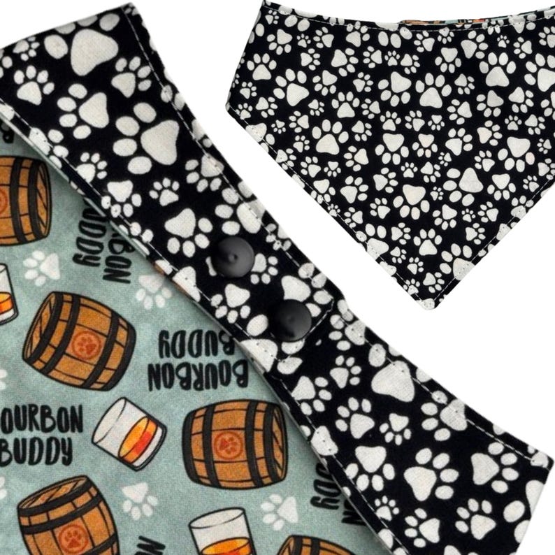 May include: Dog bandana featuring a black and white paw print design and a light blue bandana with bourbon barrel and glass graphics. The bandana has black snap closures.