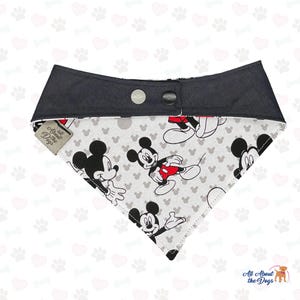 May include: Dog bandana with a Mickey Mouse pattern on a light grey background. The top section is black with two snap fasteners. The tag reads "All About the Dogs".