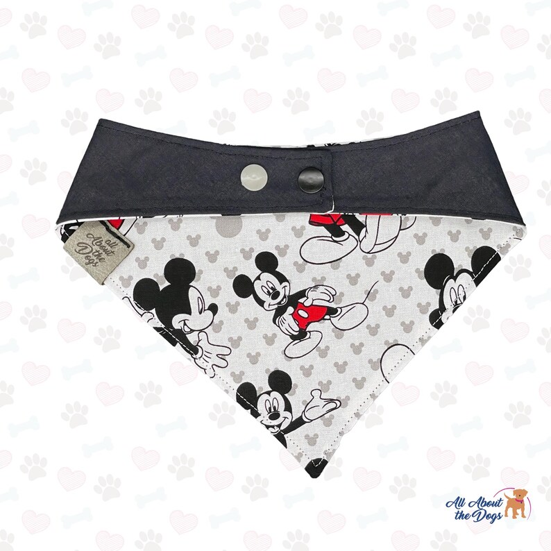 May include: Dog bandana with a Mickey Mouse pattern on a light grey background. The top section is black with two snap fasteners. The tag reads "All About the Dogs".
