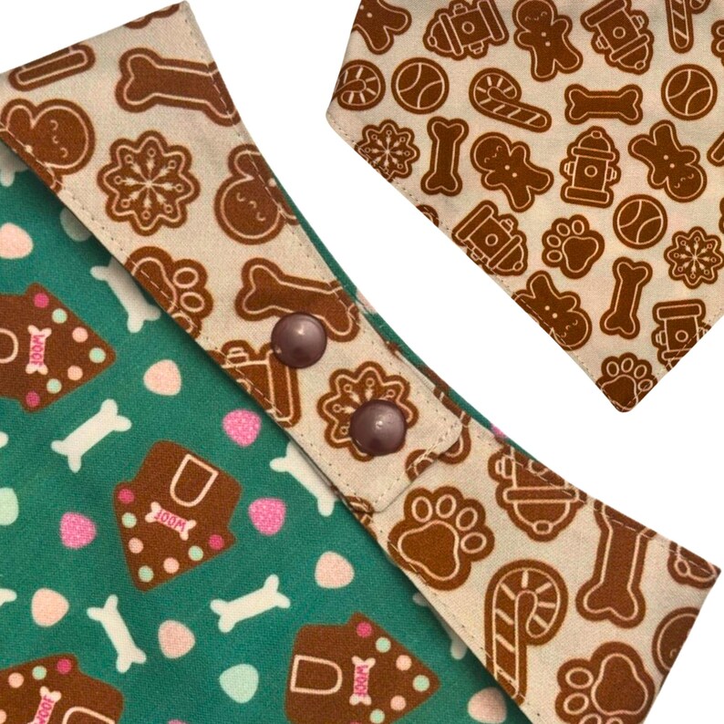 K&ouml;nnte beinhalten: Zwei Hunde-Bandanas mit festlichem Lebkuchen-Thema. Eines ist gr&uuml;n mit Knochen- und Lebkuchenhaus-Designs, das andere ist beige mit Lebkuchenm&auml;nnern, Knochen und Pfotenabdr&uuml;cken. Beide haben braune Druckkn&ouml;pfe.