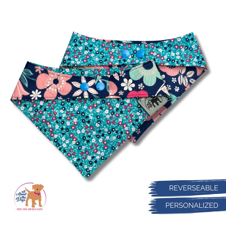 K&ouml;nnte beinhalten: Zwei wendbare Hundebandanas. Eines zeigt ein t&uuml;rkisfarbenes Blumenmuster mit rosa und wei&szlig;en Akzenten. Die andere Seite hat ein marineblaues Blumenmuster mit rosa und wei&szlig;en Blumen. Jedes Bandana hat blaue Knopfverschl&uuml;sse. Die Bandanas sind personalisiert.