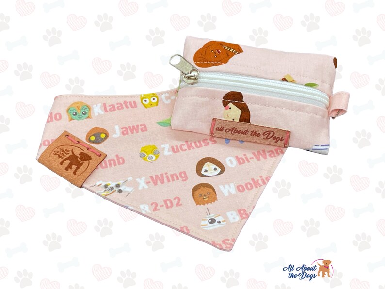 May include: A pink dog bandana and matching zippered pouch featuring Star Wars characters and text. The bandana and pouch have a repeating pattern of paw prints. The bandana has a leather tag that says "All About the Dogs".
