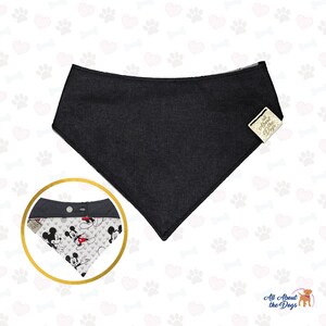 May include: A black dog bandana with a contrasting Mickey Mouse print. The bandana has a snap closure and a tag that reads "All About the Dogs". The bandana is a triangle shape.