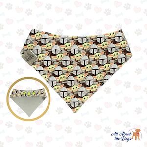 May include: A brown and tan bandana with a repeating pattern of a green alien character wearing a helmet. The bandana has a grey underside with green buttons. The bandana is labelled "All About the Dogs".