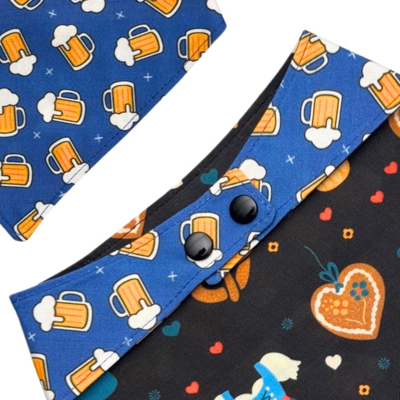 K&ouml;nnte beinhalten: Zwei Hunde-Bandanas. Eines ist blau mit gelben Bierkr&uuml;gen, das andere ist schwarz mit Lebkuchenherzen und einem blau-wei&szlig;en Design. Beide Bandanas haben schwarze Druckkn&ouml;pfe.