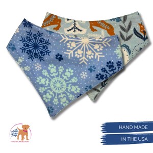 May include: Two dog bandanas. One is light blue with snowflakes and paw prints. The other is light blue with a pattern of dogs and floral designs. The bandanas are hand made in the USA.