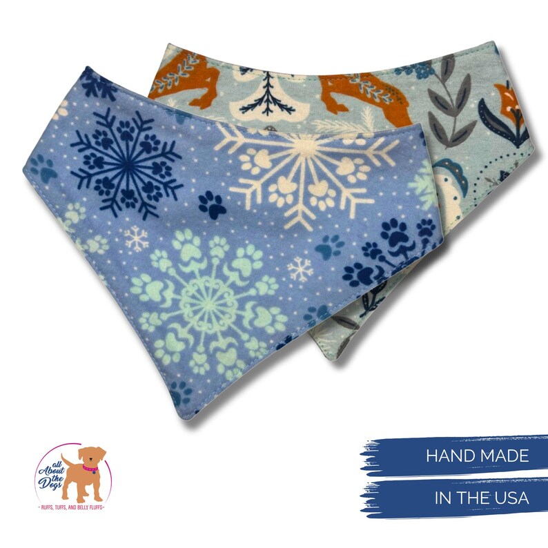 May include: Two dog bandanas. One is light blue with snowflakes and paw prints. The other is light blue with a pattern of dogs and floral designs. The bandanas are hand made in the USA.