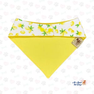 Pu&ograve; includere: Un bandana giallo per cani con un bordo superiore bianco con un motivo a limoni. Il bandana ha una forma triangolare e un'etichetta con un'illustrazione di cane. Lo sfondo &egrave; bianco con impronte di zampe.