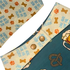 K&ouml;nnte beinhalten: Hunde-Bandana mit hellblauem Hintergrund mit Pfotenabdr&uuml;cken, Knochenformen und dem Text "JUST HERE FOR THE TREATS!". Die andere Seite ist t&uuml;rkis mit einem Bierkrug- und Brezel-Design.