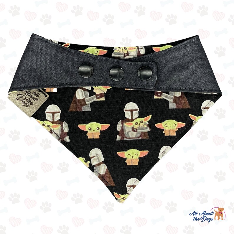 May include: Black bandana with a repeating pattern of a green alien character and a Mandalorian character. The bandana has a black snap closure and a white tag that says "All About the Dogs".