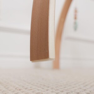 Pode incluir: Close-up de uma pe&ccedil;a de mobili&aacute;rio de madeira com uma borda curva castanho-clara e uma lateral branca. A pe&ccedil;a, provavelmente parte de uma cadeira ou mesa, mostra um design minimalista. O fundo est&aacute; desfocado, com uma paleta de cores neutras.