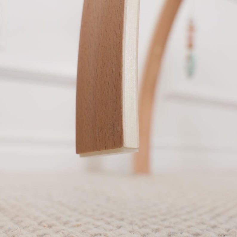 Pode incluir: Close-up de uma pe&ccedil;a de mobili&aacute;rio de madeira com uma borda curva castanho-clara e uma lateral branca. A pe&ccedil;a, provavelmente parte de uma cadeira ou mesa, mostra um design minimalista. O fundo est&aacute; desfocado, com uma paleta de cores neutras.