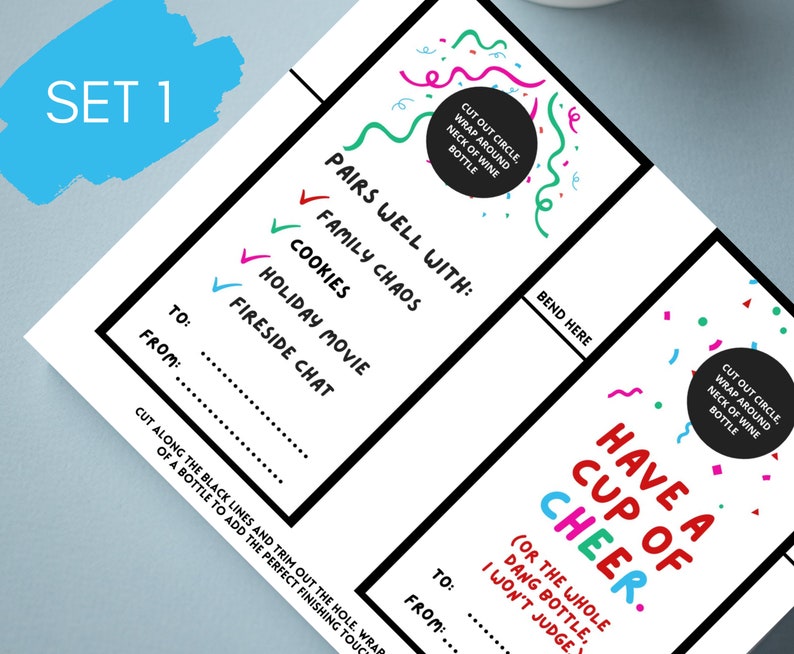 May include: Set of two white wine bottle tags with colorful text and confetti. One tag reads "Pairs well with: Family Chaos, Cookies, Holiday Movie, Fireside Chat." The other says "Have a Cup of Cheer."