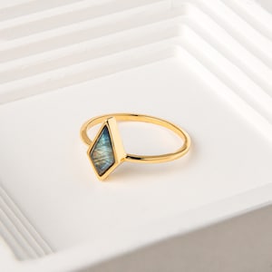 May include: A gold ring with a blue and green gemstone set in a diamond shape.