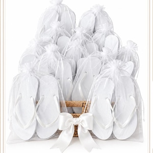 May include: A collection of white flip-flops, each individually packaged in a sheer white organza drawstring bag. The bags are arranged in a woven wicker basket, which is decorated with a large, smooth white satin ribbon bow at the front.