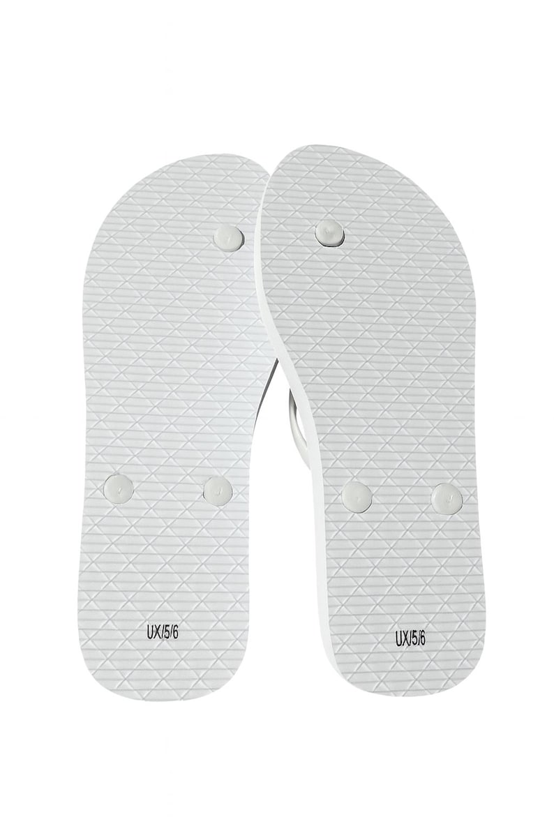 May include: A pair of white flip-flops featuring a textured diamond pattern on the footbed. Each sandal displays the text UX/5/6 printed in black near the heel area, along with three circular plug points for the toe post and strap attachments.