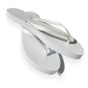 May include: A pair of solid white flip-flops featuring a textured footbed with a raised dot pattern and smooth, Y-shaped straps. The sandals are constructed from a lightweight foam material, showcasing a simple design with no additional patterns or colours.
