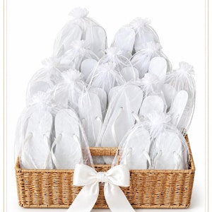 May include: A rectangular woven wicker basket filled with multiple pairs of white flip-flops, each individually packaged in a sheer white organza drawstring bag. A large white satin ribbon bow is attached to the front centre of the basket.