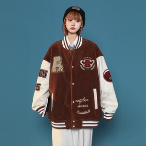 May include: Brown varsity jacket with white sleeves and striped trim. The jacket has embroidered patches with a letter A, a basketball, and the text "regular season basketball".