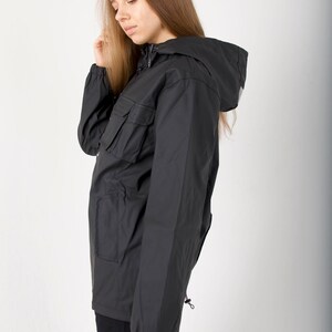 May include: A black hooded jacket with a zipper closure and a large pocket on the left side. The jacket has a drawstring at the bottom and a small loop on the right side. The jacket is made of a water-resistant material.