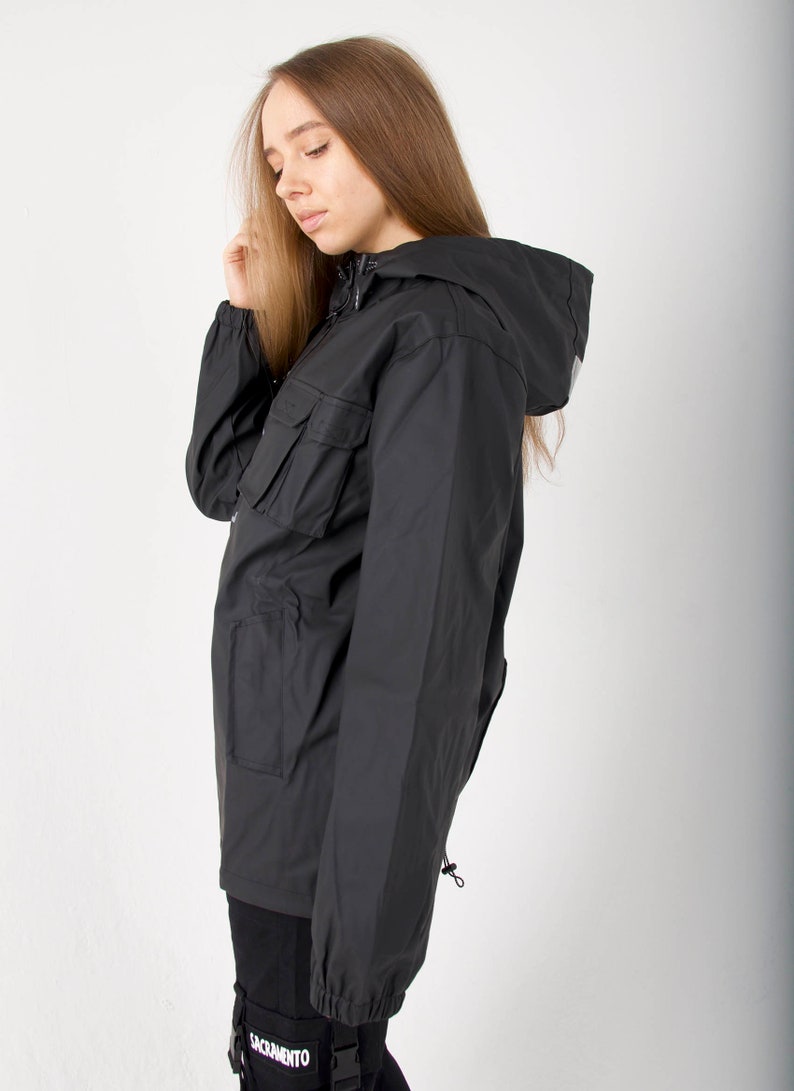 May include: A black hooded jacket with a zipper closure and a large pocket on the left side. The jacket has a drawstring at the bottom and a small loop on the right side. The jacket is made of a water-resistant material.